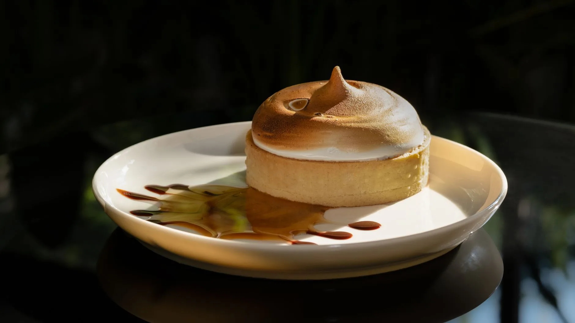 Lemon meringue tart with caramel sauce on a white plate.