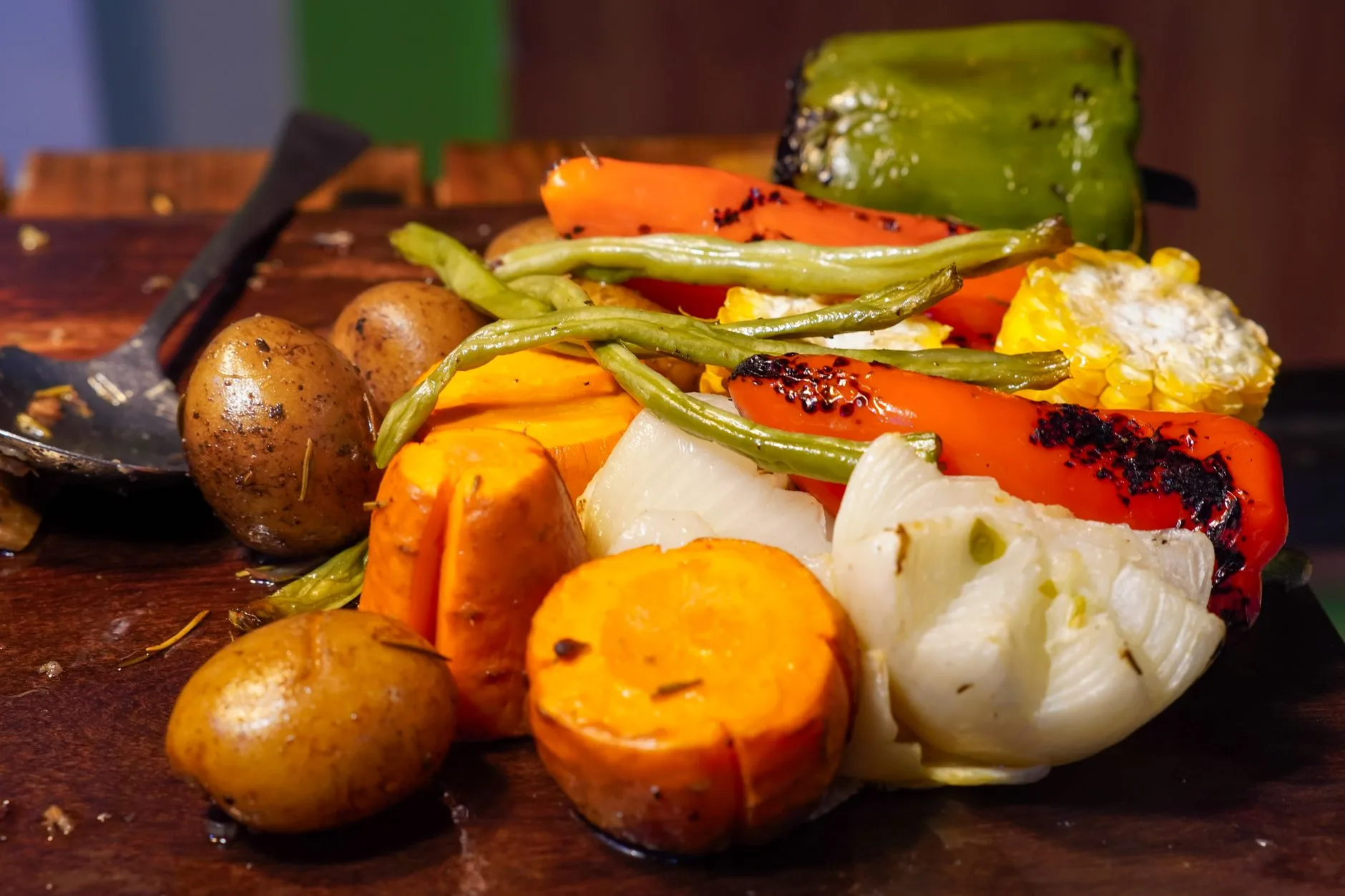 A vibrant assortment of grilled vegetables including bell peppers, beans, and potatoes on a wooden board.