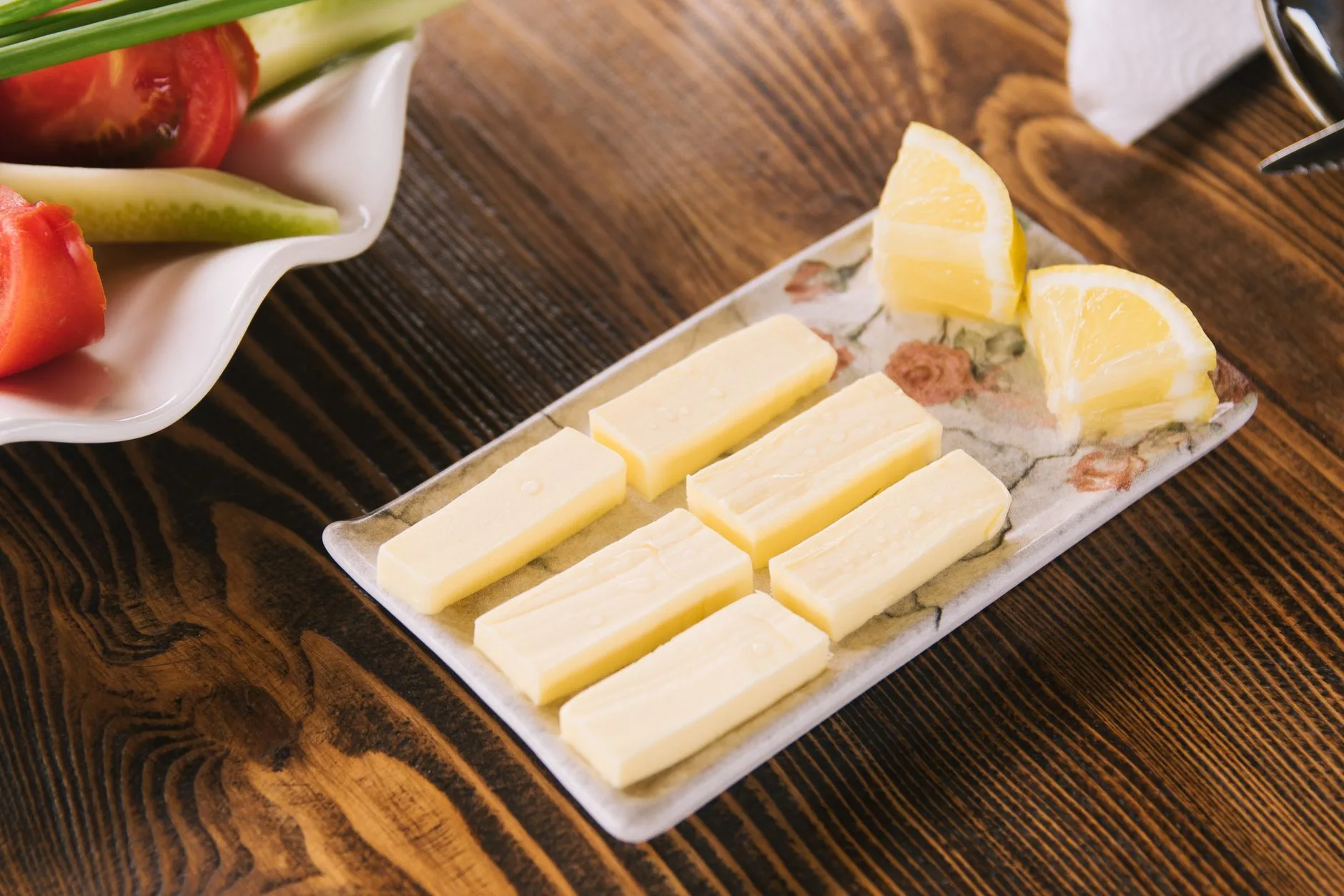 Butter sticks and lemon slices on a floral tray on a wooden table. Fresh ingredients for cooking.